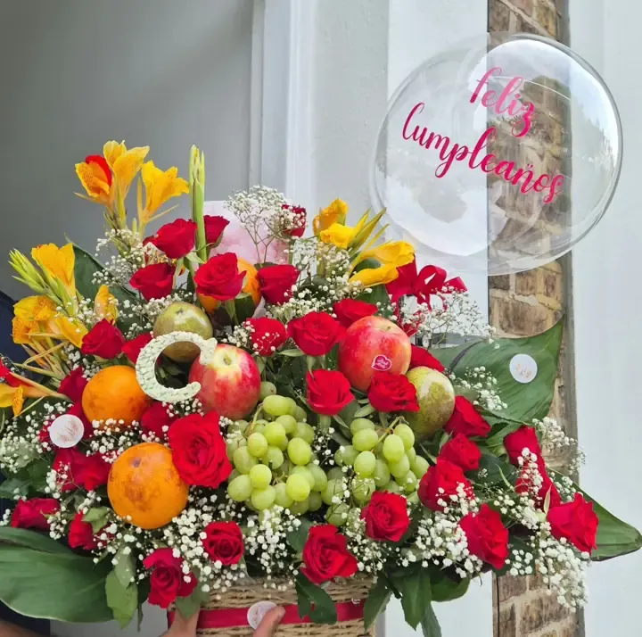 Fruit basket with red roses, grapes, apples, oranges and a Feliz Cumpleaños balloon, London