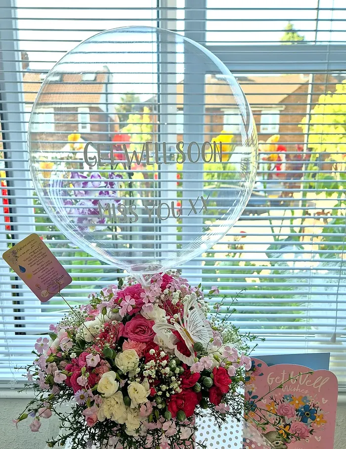 Get well soon balloon over a pink and white flower gift box with a butterfly