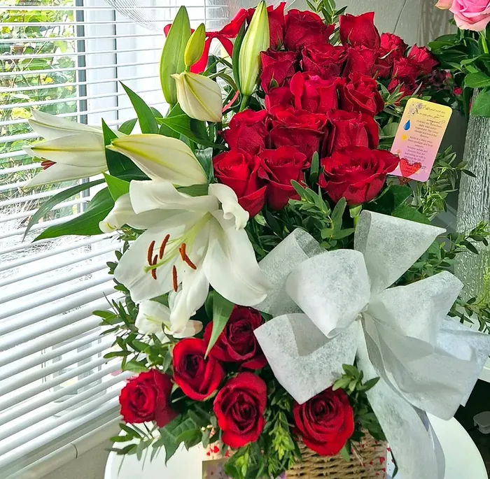 Red roses and white lilies in a basket with a white ribbon bow