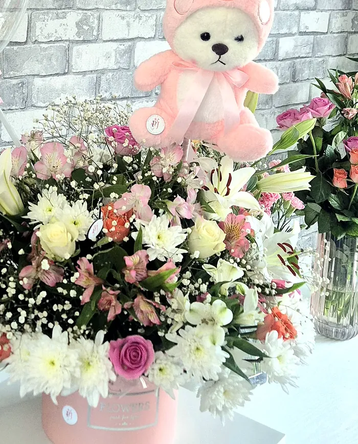Pink teddy bear on a flower gift box with white chrysanthemums and roses