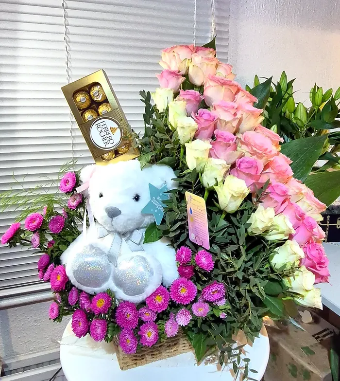 White teddy bear and Ferrero Rocher with pink and cream roses in a gift basket
